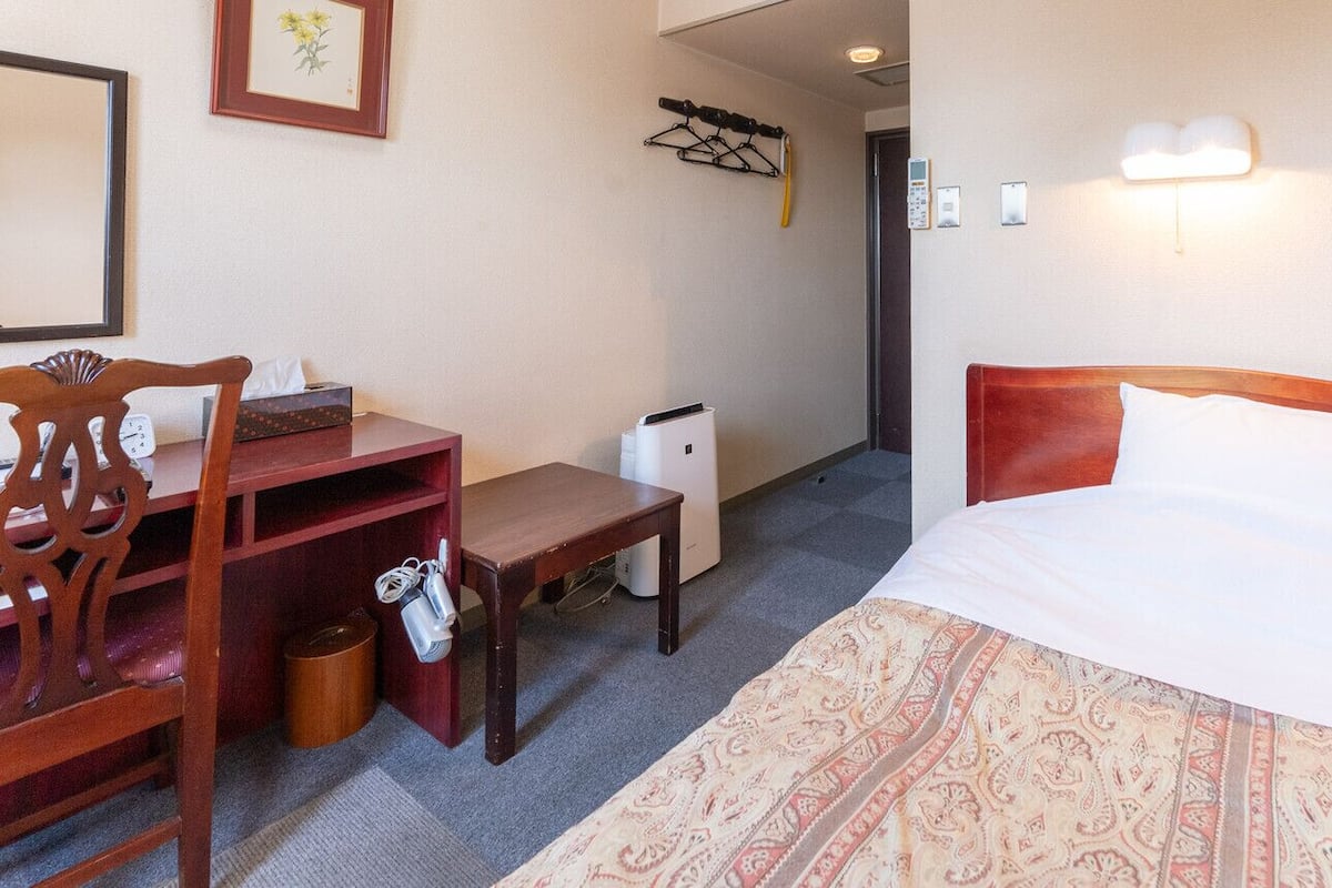 Une chambre d’hôtel équipée d’un lit, d’un bureau, d’une chaise, d’une poubelle et d’un porte-manteau.