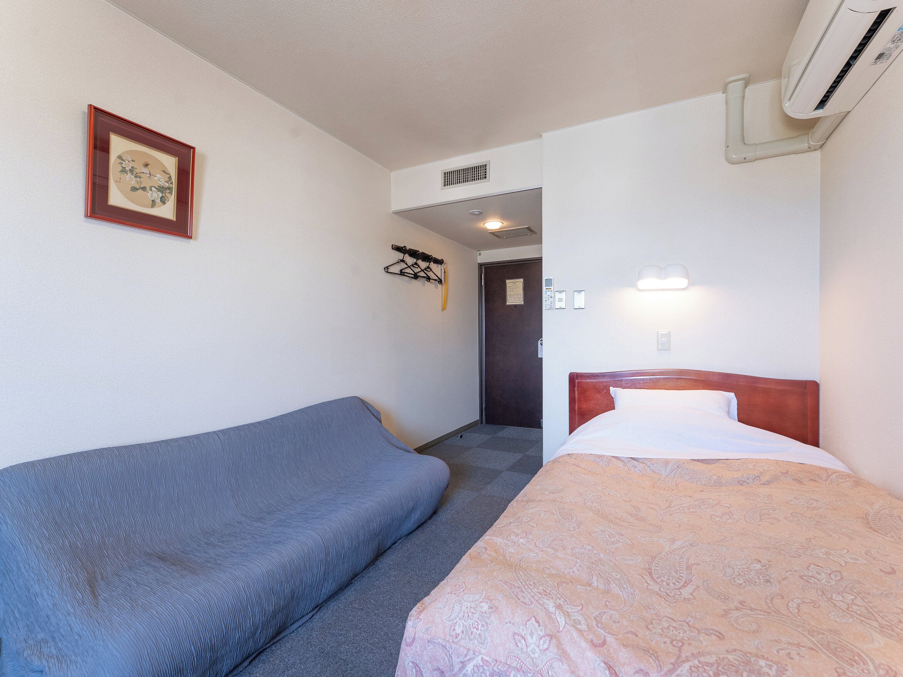 Habitación de hotel con un sofá azul, una cama con colcha estampada y un equipo de aire acondicionado en la pared.