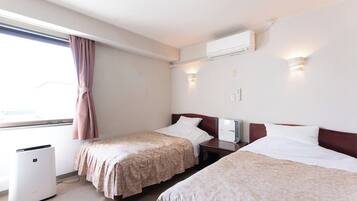 A hotel room with two beds, a window with curtains, an air conditioning unit, and a bedside table with a lamp.