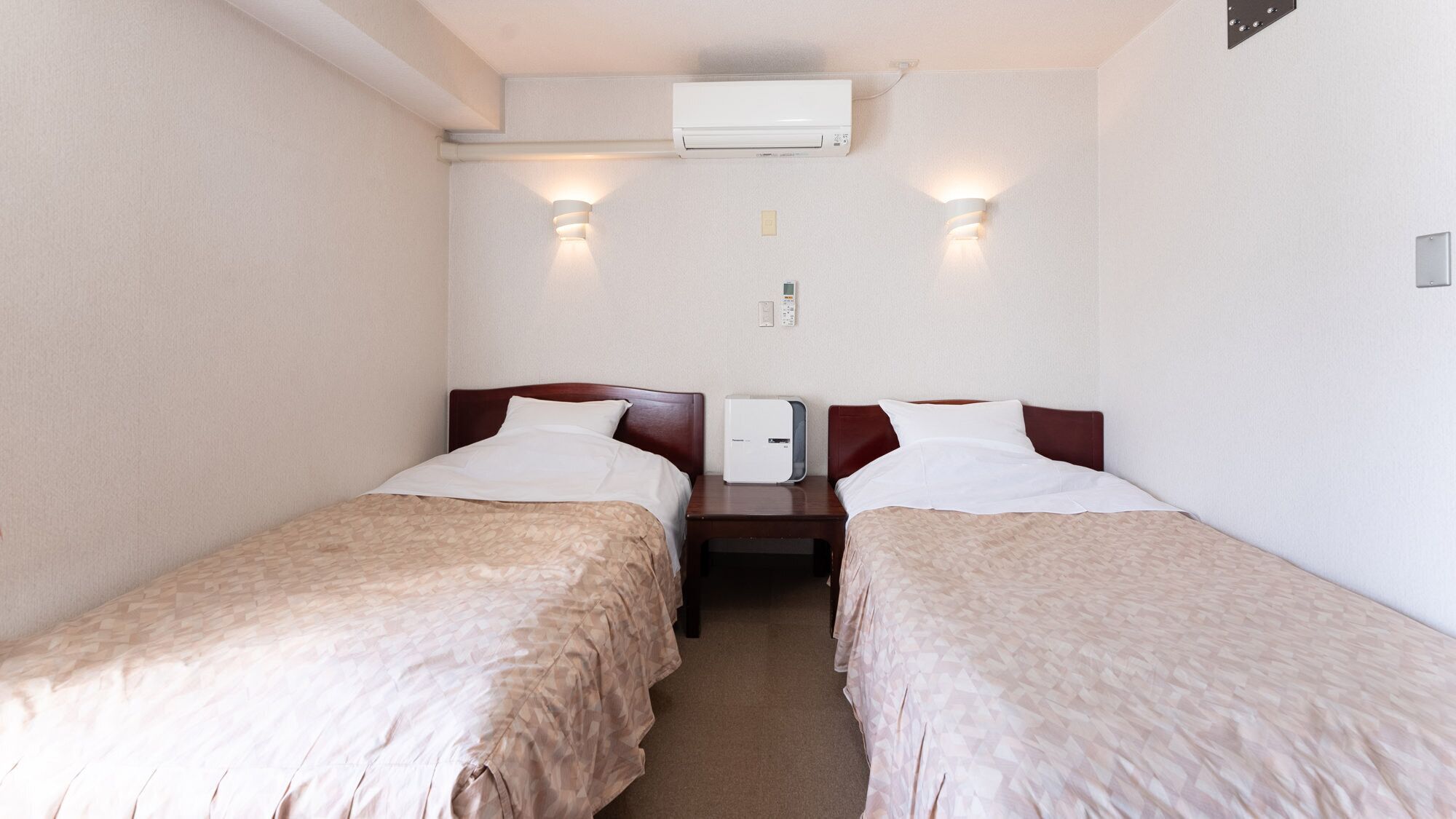 Habitación de hotel con dos camas, aire acondicionado instalado en la pared y una mesita de noche con lámpara.