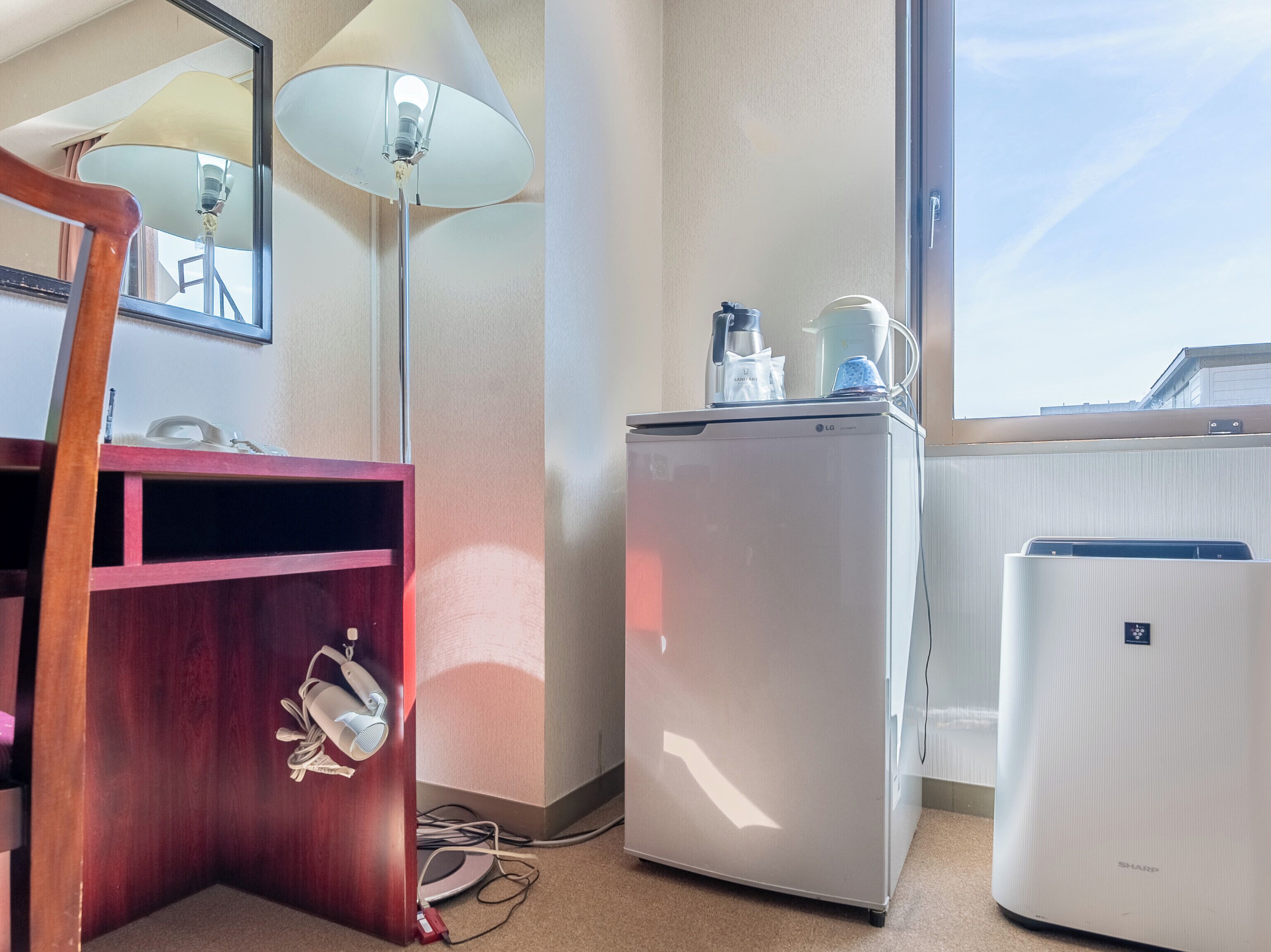 Habitación de hotel con escritorio de madera, refrigerador compacto, microondas y ventana con vista al cielo.