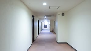 Un pasillo largo y estrecho con puertas a ambos lados, iluminación empotrada y un extintor cerca del final.