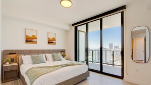 A modern bedroom with a large bed, a nightstand, a mirror, and a city view through a sliding door. - Oceanview Corner 2BR/2BA in Miami Beach + Beach Club 1710GP (Miami Beach)