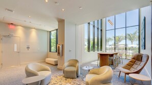 A modern lobby with a seating area, a small table, and large windows offering a view of palm trees. - Oceanview Corner 2BR/2BA in Miami Beach + Beach Club 1710GP (Miami Beach)