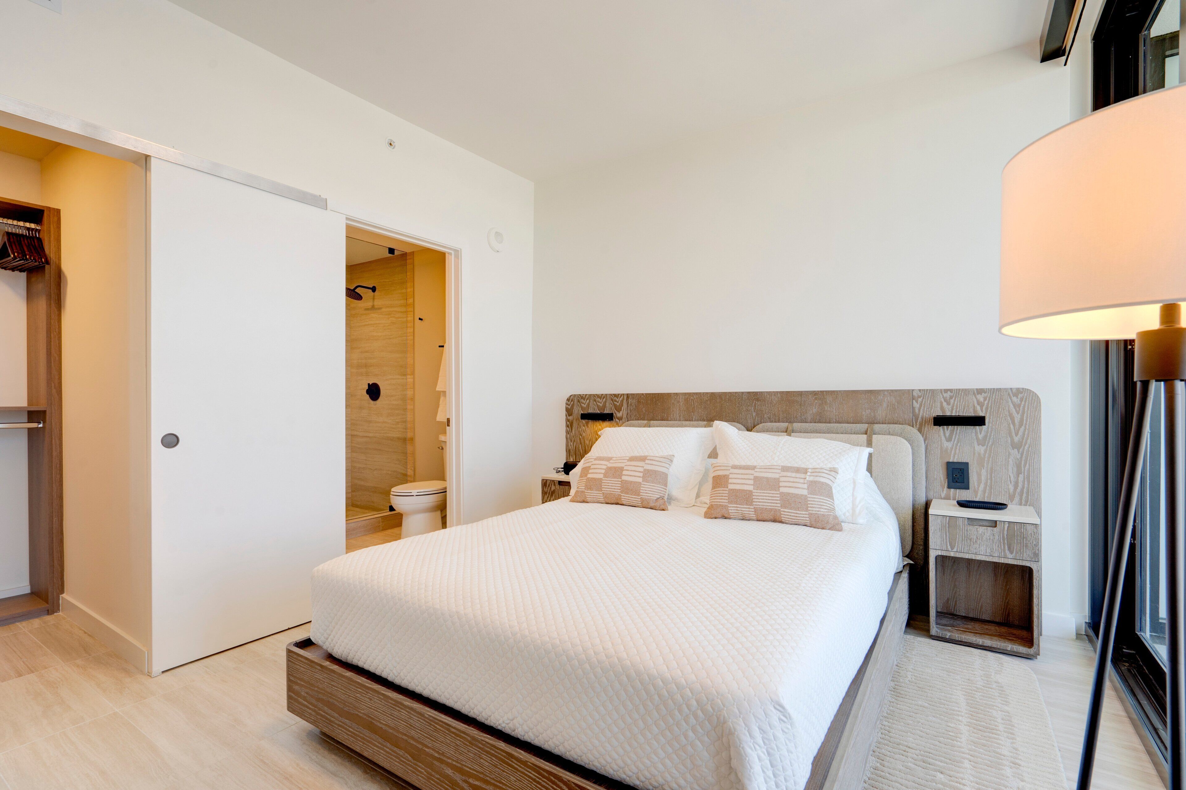 A modern bedroom with a large bed, a wooden headboard, a bedside table, and a nightstand.
