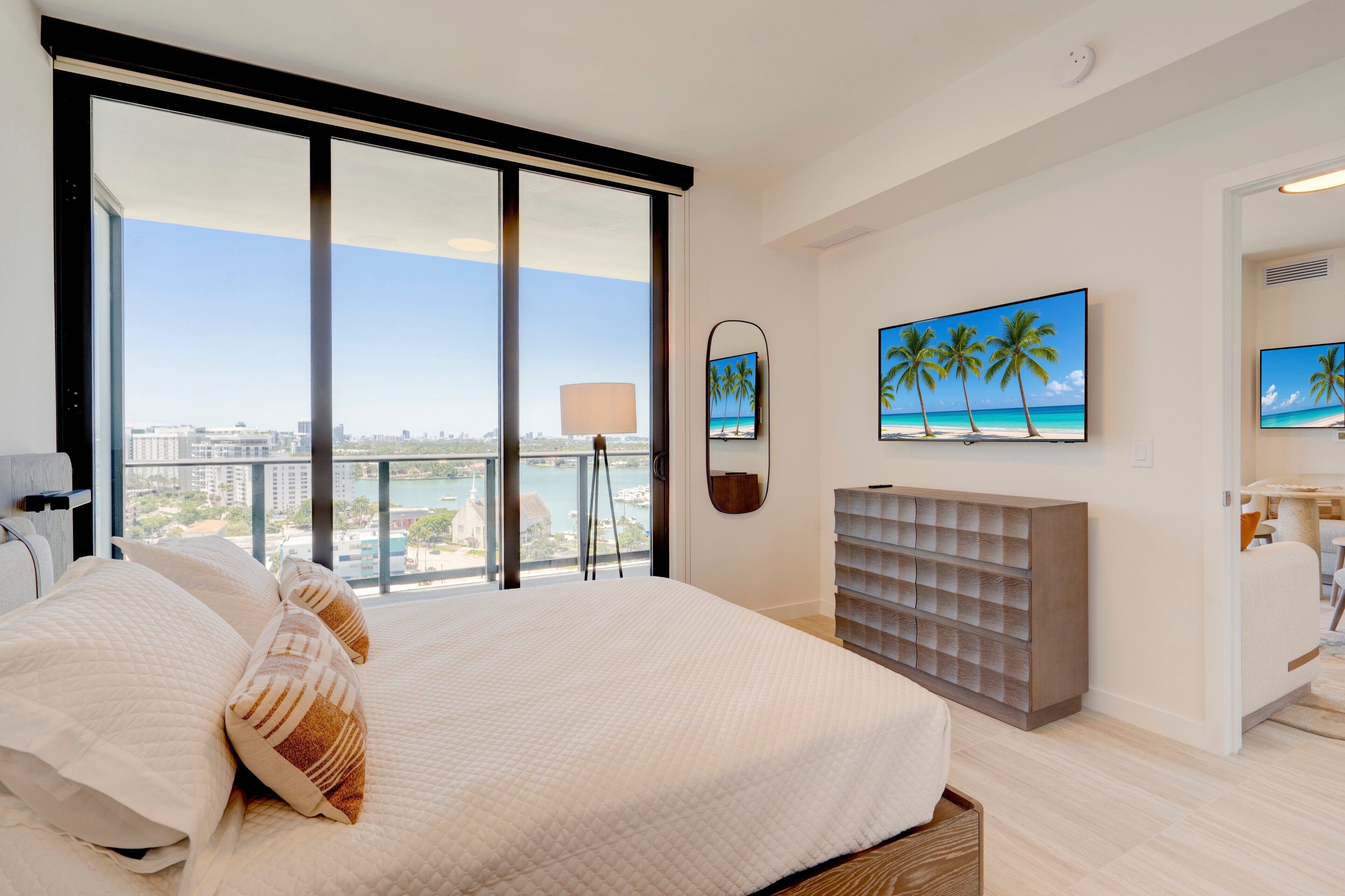 A modern hotel room with a large bed, a view of the city, and a balcony with a view of the ocean.