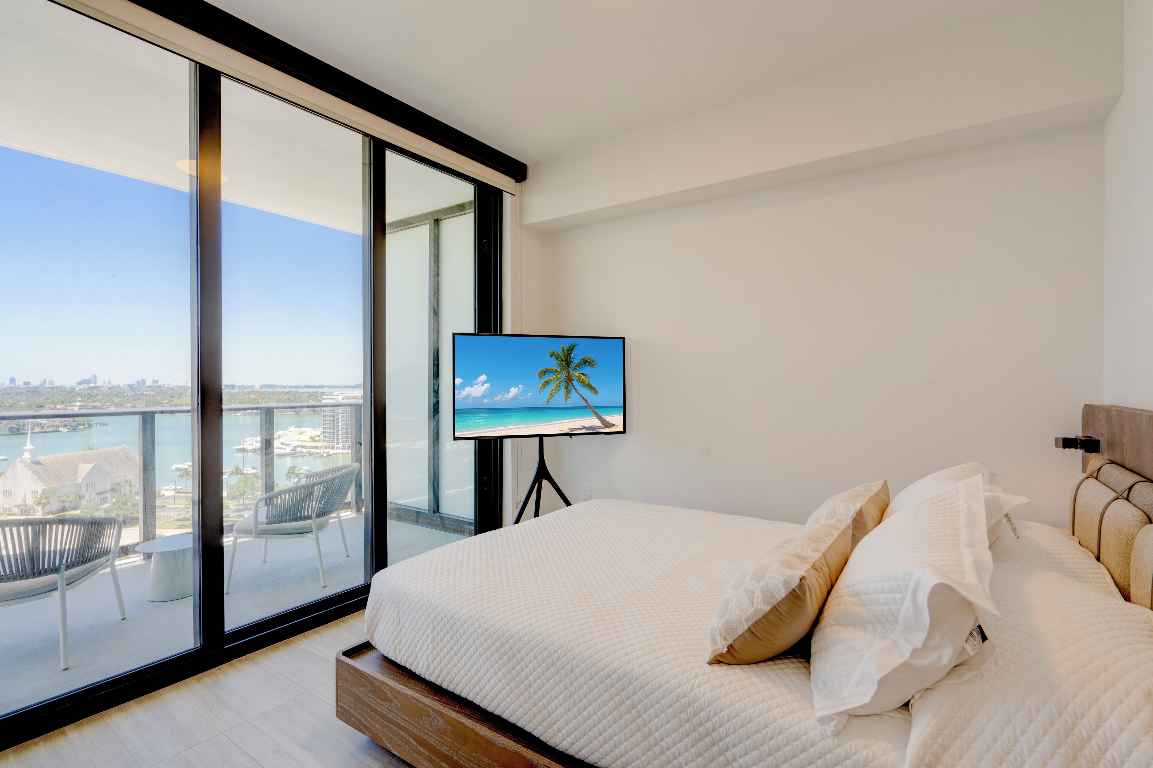Una camera da letto con un'ampia finestra, un letto e una televisione che mostra una spiaggia.