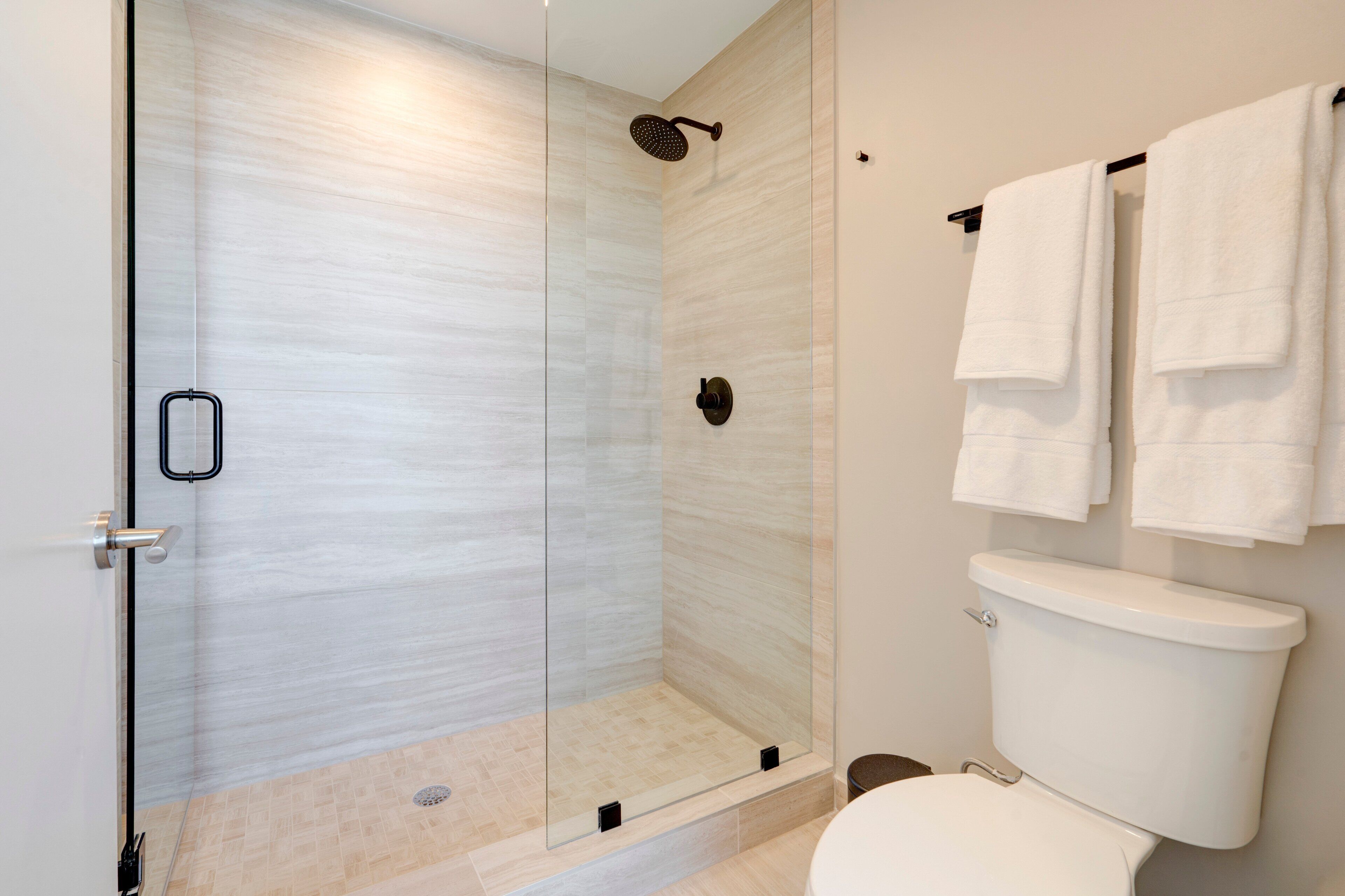 A modern bathroom with a glass-enclosed shower, a toilet, and a towel rack with multiple towels.