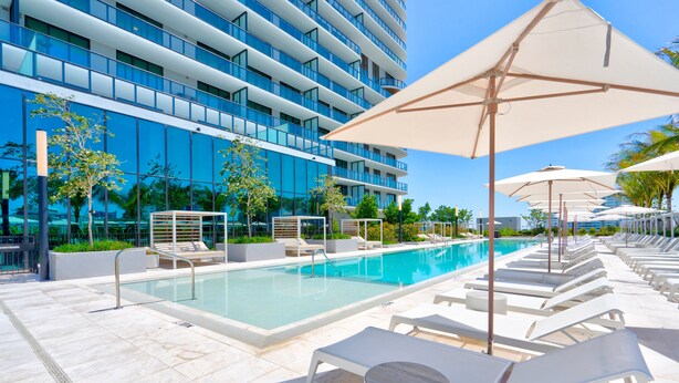 A modern hotel pool area with a clear blue pool, white sun loungers, and umbrellas. - Oceanview 2BR/2BA in Miami Beach + Beach Club 1408RP (Miami Beach)