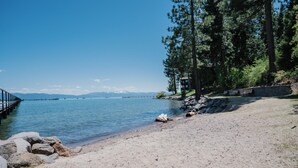 A sandy beach with a rocky shoreline, a wooden pier extending into calm water, and a stone structure with benches.