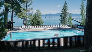 A pool with a view of the lake and mountains, surrounded by trees and a wooden deck.