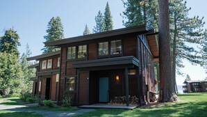 A modern two-story house with large windows, a covered porch, and a view of the surrounding forest.