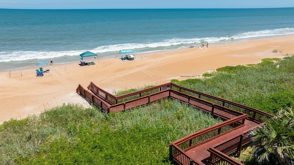 Ein Strand mit einer Holzpromenade, die zum Ufer führt, feinem Sand und einem klaren, blauen Meer.