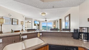 A modern kitchen with granite countertops, a built-in dishwasher, a coffee maker, and a view of the ocean. - Direct oceanfront corner 2/2 with stunning views, huge balcony, heated pool, and garage parking (Ormond Beach)