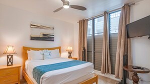 A bedroom with a bed, two bedside tables with lamps, a ceiling fan, a TV, and a window with curtains.