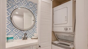 A compact bathroom with a sink, mirror, and a wall-mounted washing machine.