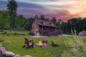 Una casa con porche, un brasero y tres sillas Adirondack.