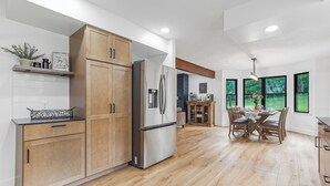Una cocina moderna con armarios de madera, un refrigerador de acero inoxidable y un comedor con mesa y sillas.