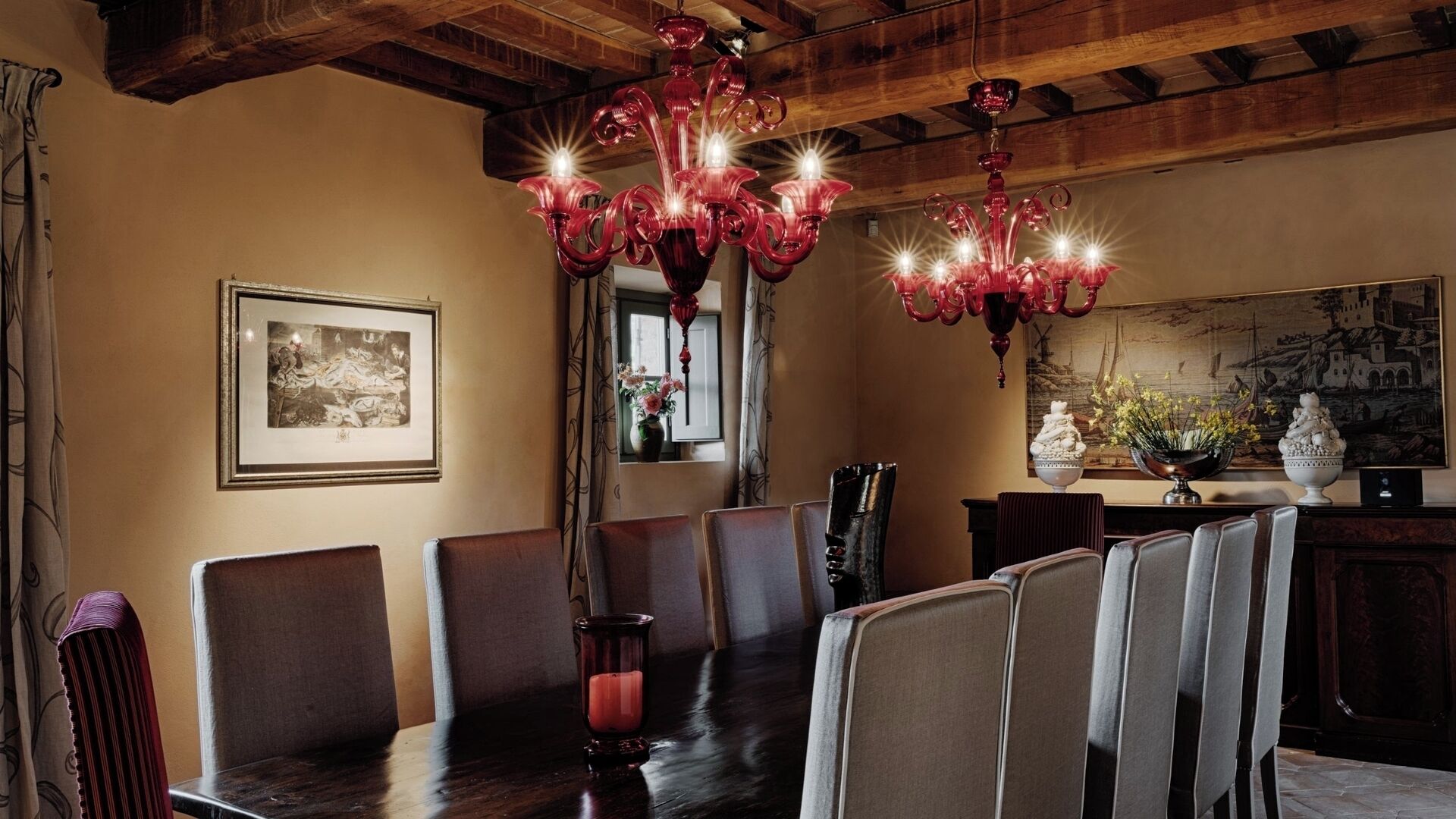 Uma sala de jantar com uma longa mesa de madeira, várias cadeiras e um candelabro com diversas lâmpadas.