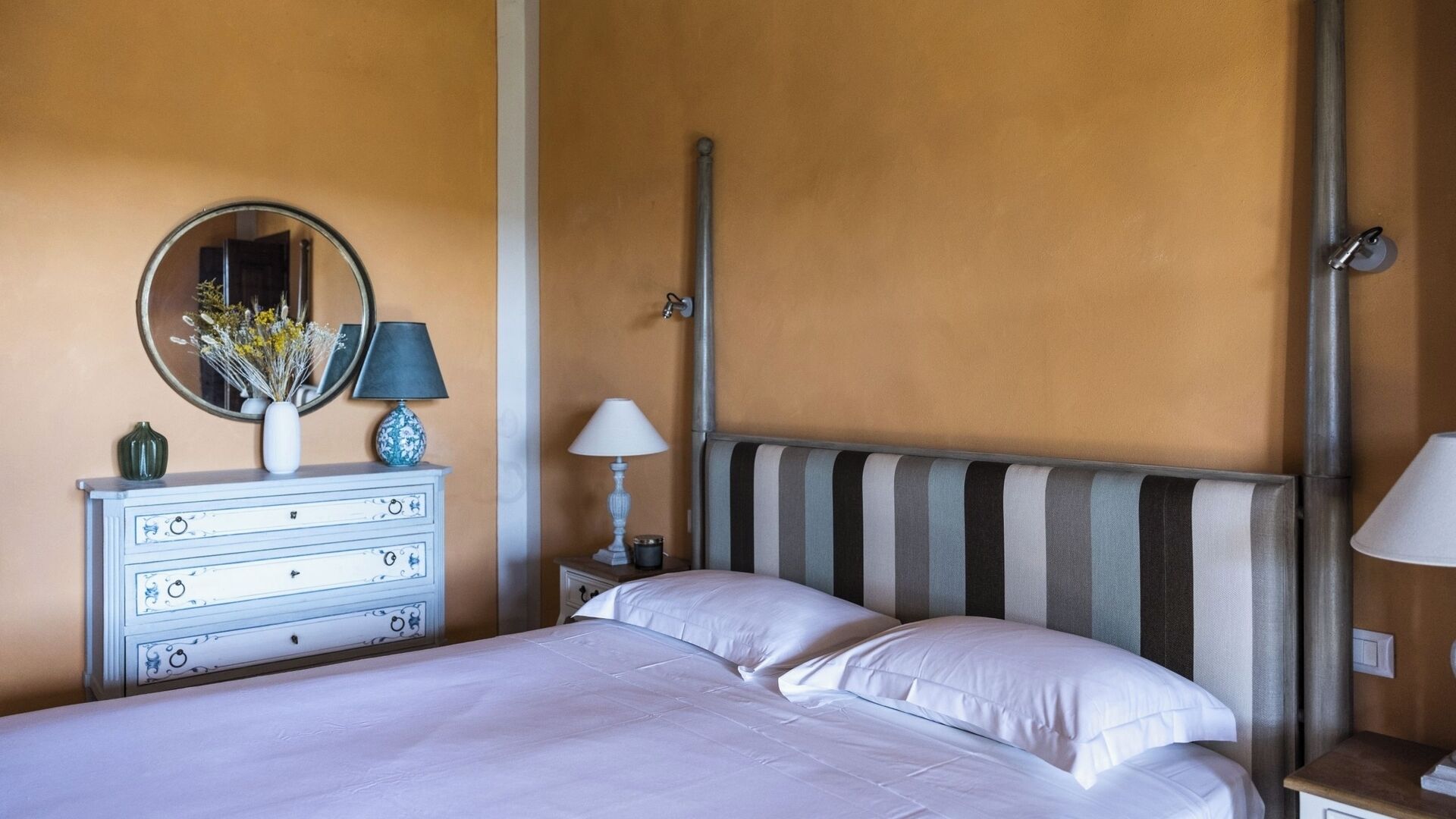 A hotel room with a bed, a dresser, a mirror, and a nightstand with lamps.
