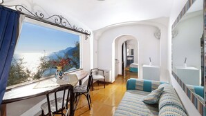 A modern room with a large window, a dining area, a sofa, and a bathroom visible through an archway. - Casa Dalila, walking distance from Positano (Provincia di Salerno)