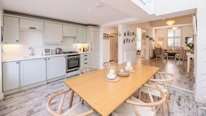 A spacious kitchen with white cabinets, a wooden dining table, and a view into the living area.