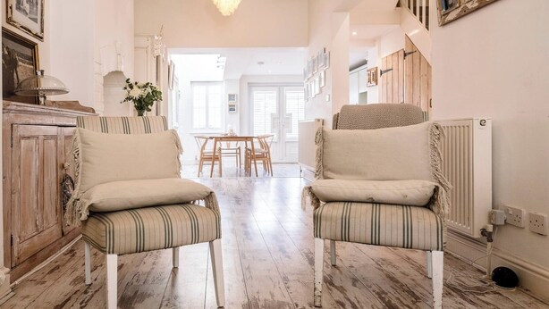 A spacious room with two upholstered chairs, a wooden floor, a dining table with chairs, and a chandelier.