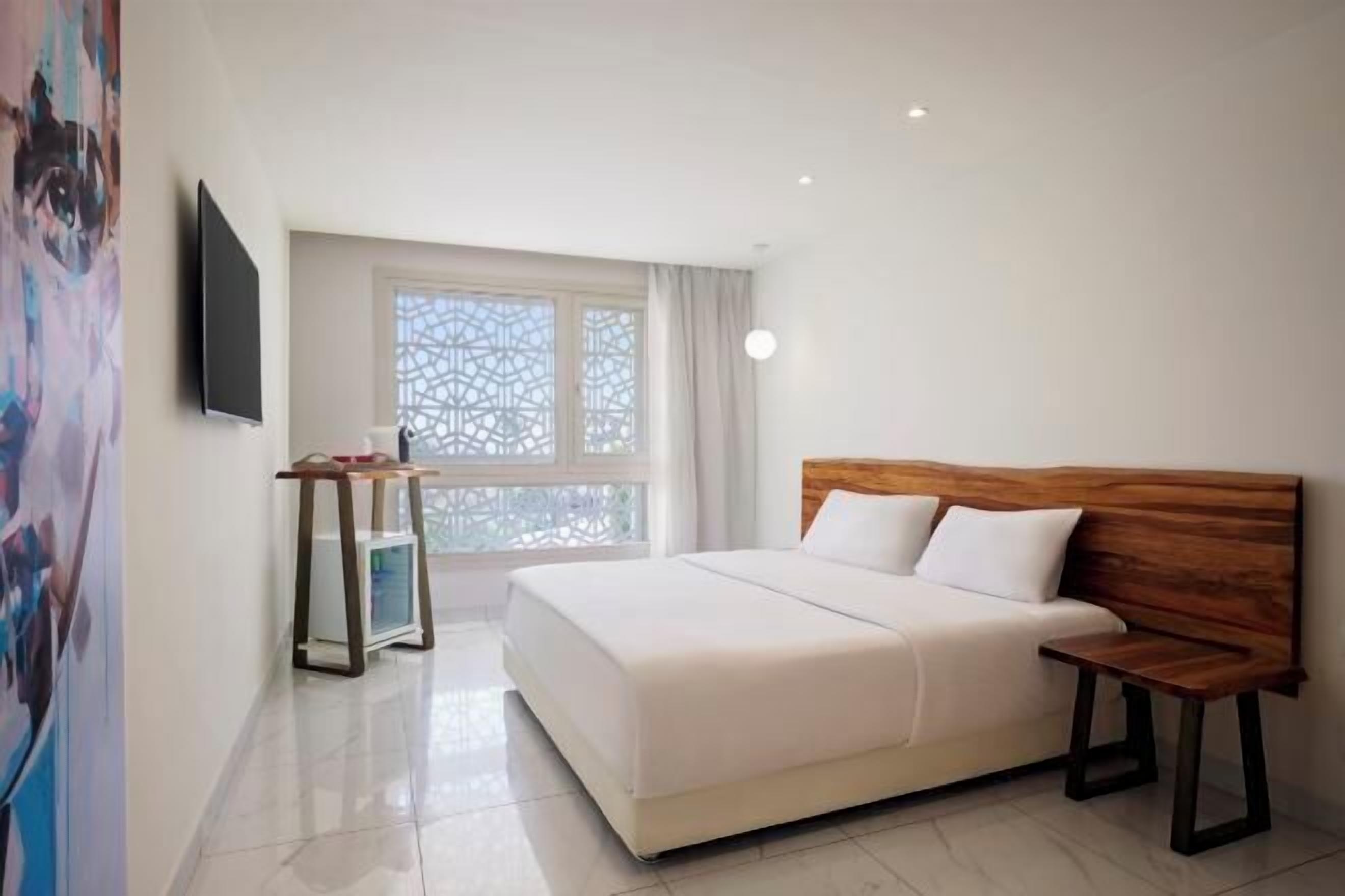 Una habitaci ón de hotel con cama, mesita de noche, un escritorio pequeño y ventana con vistas.