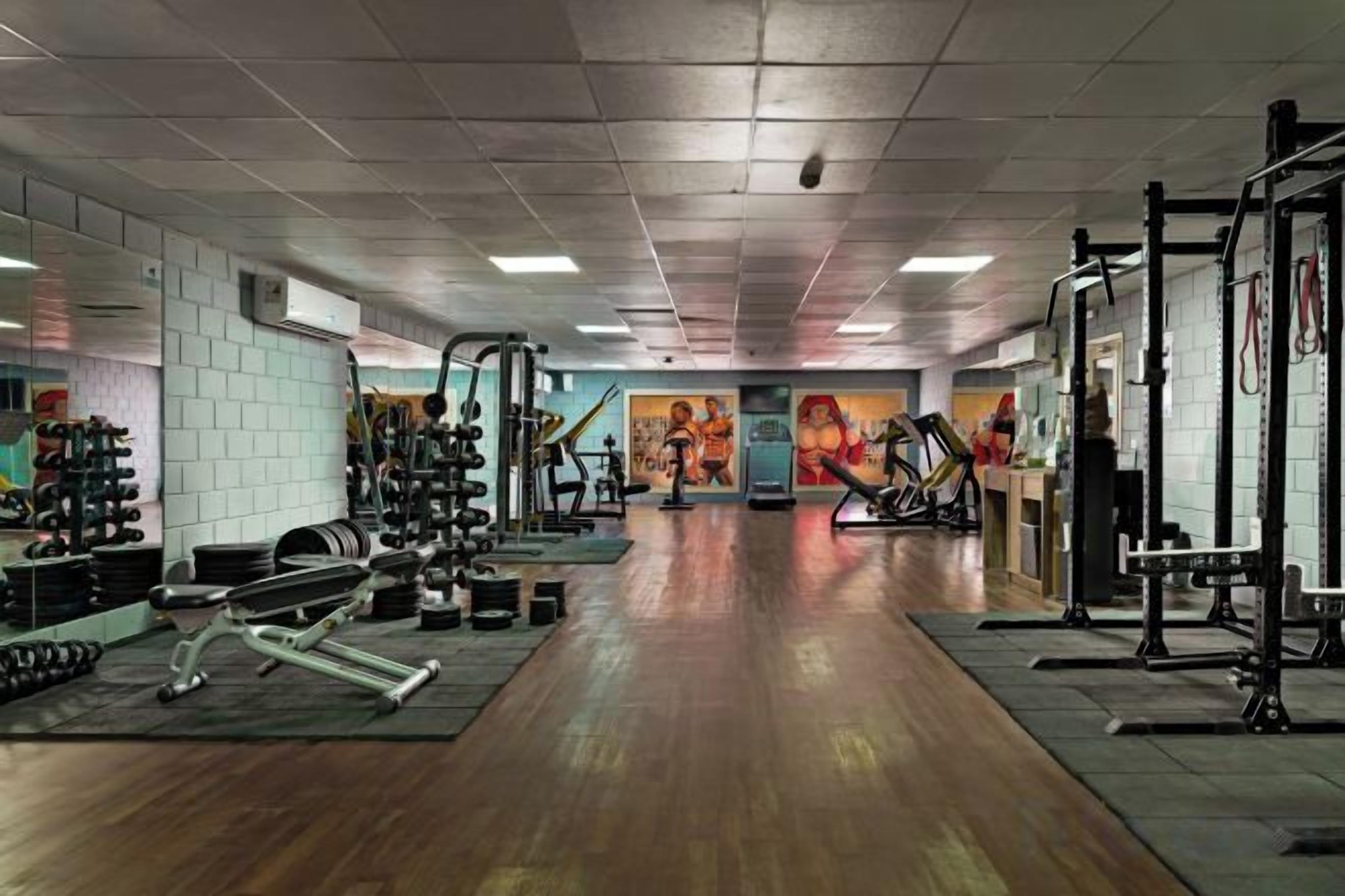 A gym with weightlifting equipment, treadmills, and a mirrored wall.