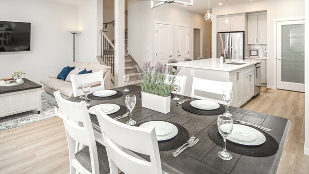 Een moderne keuken met witte kasten, een roestvrijstalen koelkast en een eethoek met een donker houten tafel en witte stoelen.