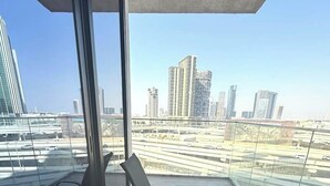 Un balcon avec une table et des chaises en verre, donnant sur un paysage urbain composé d’immeubles modernes et d’une autoroute.