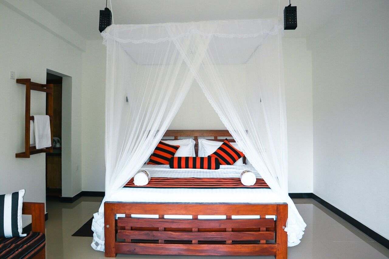 A bed with a wooden frame and white bedding, a white canopy, and striped pillows.