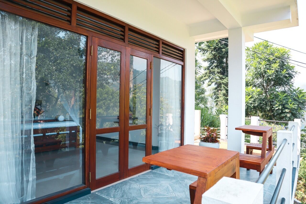 A balcony with a wooden table and chairs, a sliding glass door, and potted plants.