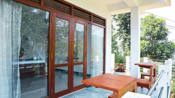 A balcony with a wooden table and chairs, a sliding glass door, and potted plants.