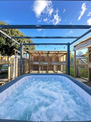 Ein Außenbereich mit Whirlpool und einer hölzernen Pergola, umgeben von einem eingezäunten Garten.