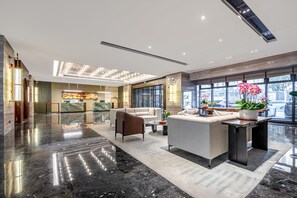 Een moderne lobby met een receptiebalie, een zithoek en grote ramen.