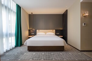 Habitación de hotel moderna con una cama grande, una mesita de noche, una lámpara y vistas a la ciudad a través del ventanal.