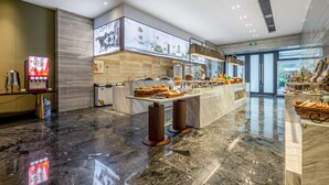 Un hall d’hôtel moderne avec un sol en marbre, un comptoir d’accueil, un écran numérique et une grande fenêtre donnant sur l’extérieur.