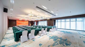 A conference room with rows of tables, white chairs, and a large screen.