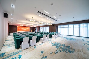 Una sala conferenze con file di tavoli, sedie bianche e un grande schermo.