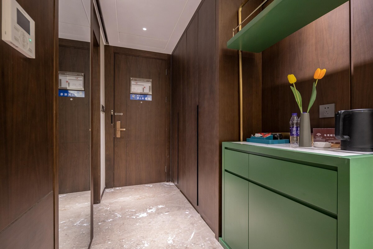 A hallway with wooden doors, a green counter with a vase of flowers, and a coffee machine.