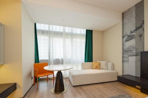 Een moderne hotelkamer met een bank, een eettafel en een groot raam met gordijnen.