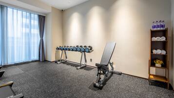 A gym with exercise equipment, a bench, and a shelf with towels and water bottles.
