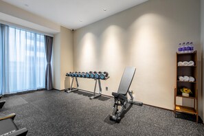 Uma academia com equipamentos de ginástica, um banco e uma estante com toalhas e garrafas de água.