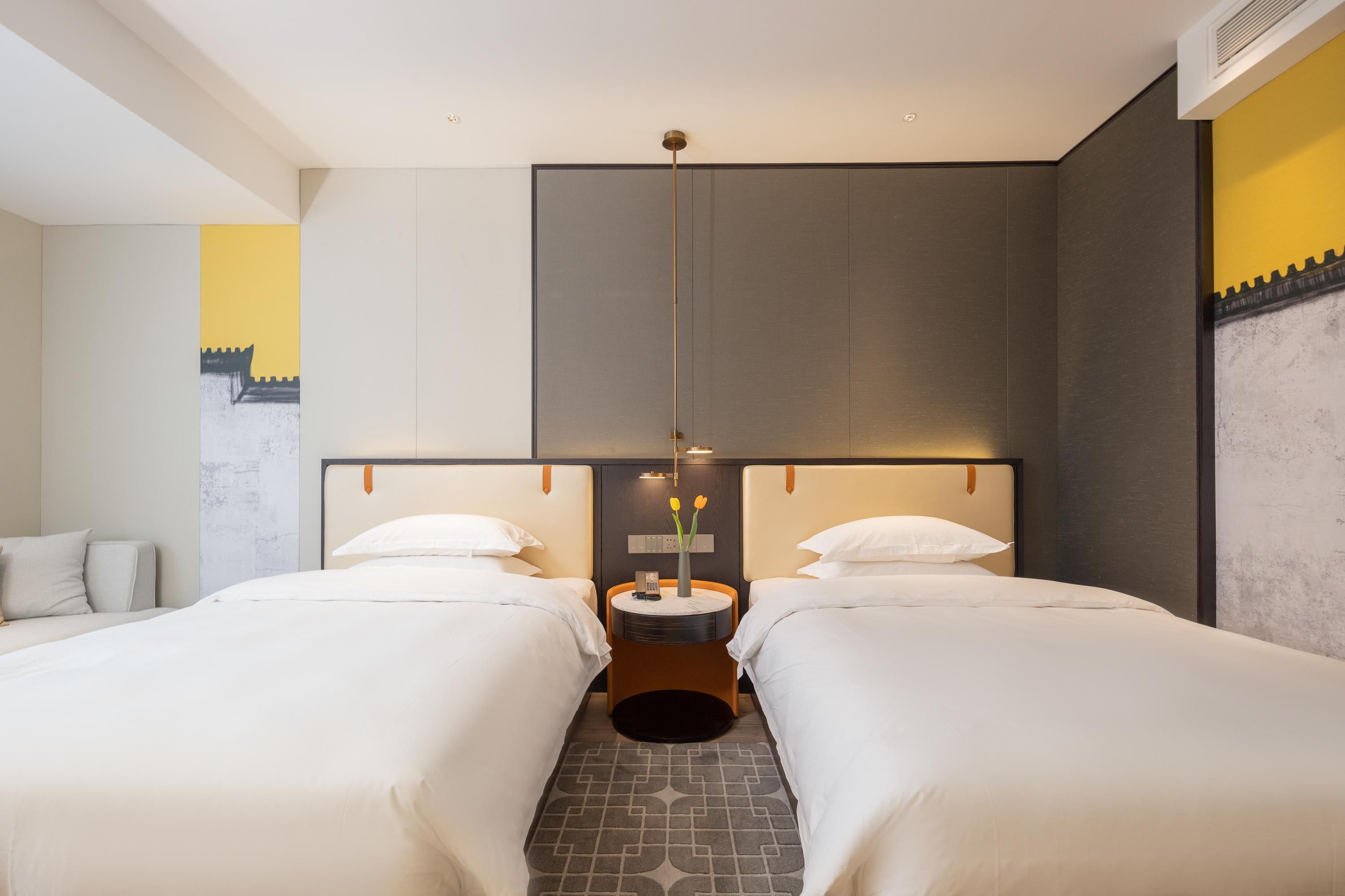 A hotel room with two beds, a round table with a vase of flowers, and a modern light fixture.