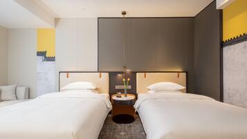 A hotel room with two beds, a round table with a vase of flowers, and a modern light fixture.
