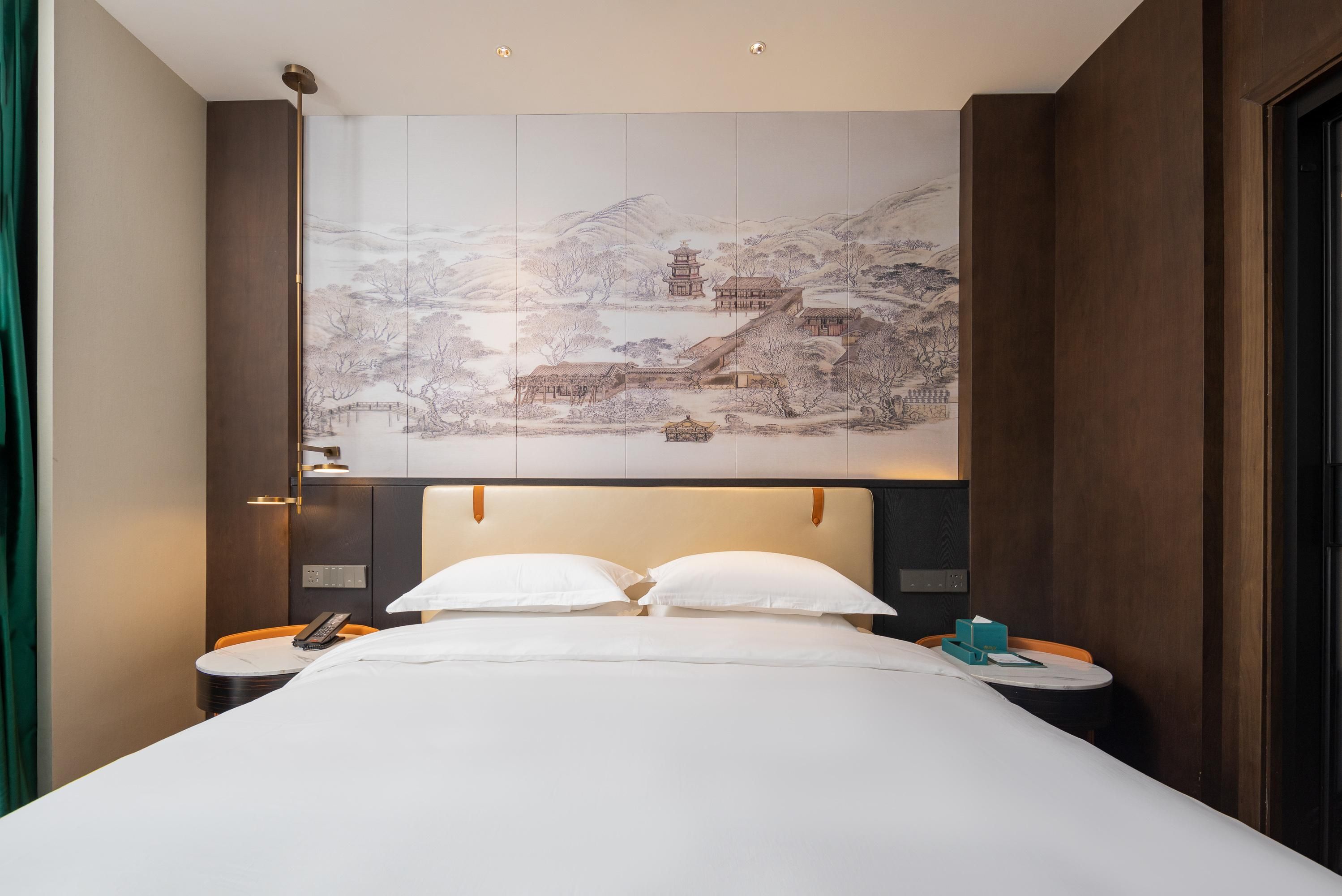 Habitació d'hotel amb un llit gran, dues taules de nit, una obra penjada a la paret que representa una escena tradicional, i un panell de fusta al capçal del llit.