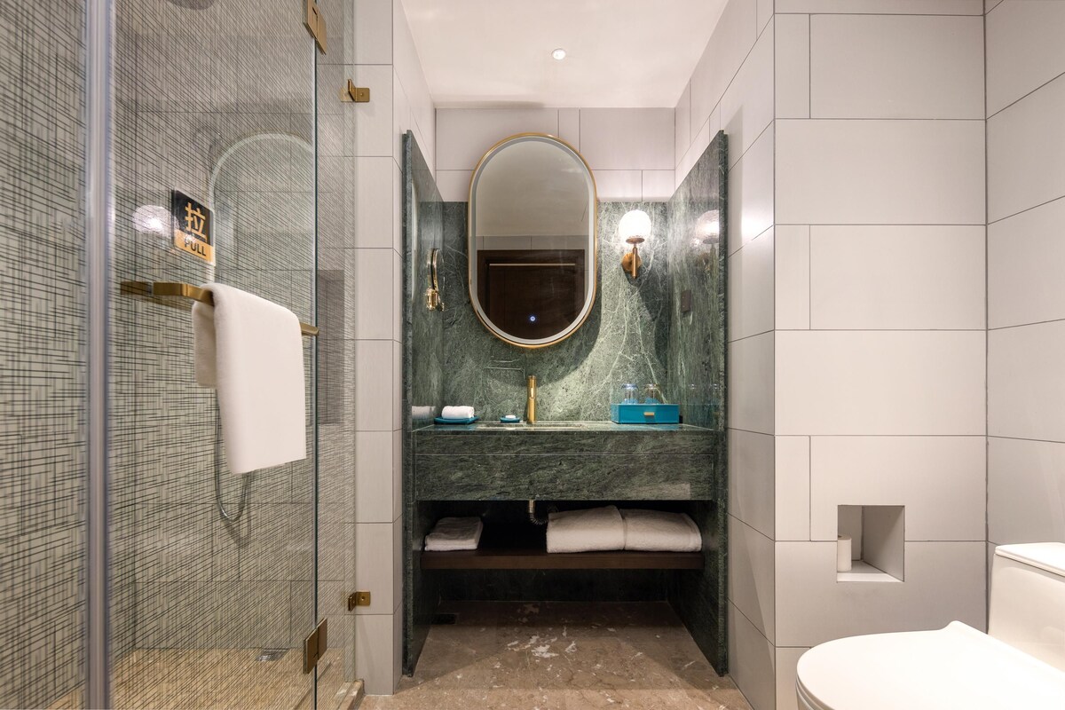Un baño moderno con ducha de vidrio, tocador de mármol, un espejo grande y un inodoro.