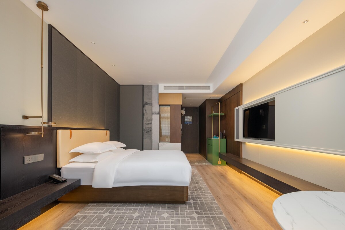 A modern hotel room with a large bed, bedside table, and a TV mounted on the wall.