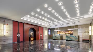 A modern lobby with a marble floor, a reception desk, and a digital screen displaying information.